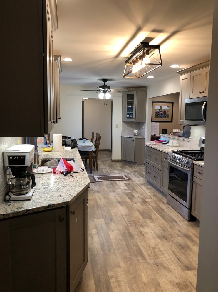 Photo of a large country galley eat-in kitchen in Chicago with an undermount sink, shaker cabinets, grey cabinets, quartzite benchtops, grey splashback, glass tile splashback, stainless steel appliances, laminate floors, with island, brown floor and beige benchtop.