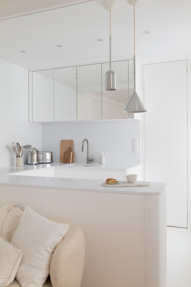 Photo of a medium sized contemporary grey and white u-shaped open plan kitchen in Paris with a single-bowl sink, beaded cabinets, white cabinets, composite countertops, white splashback, white appliances, concrete flooring, white floors and white worktops.