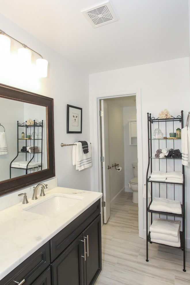 This is an example of a mid-sized transitional 3/4 bathroom in Atlanta with recessed-panel cabinets, dark wood cabinets, an alcove shower, a two-piece toilet, gray tile, porcelain tile, grey walls, porcelain floors, an undermount sink, marble benchtops, grey floor, a sliding shower screen and white benchtops.