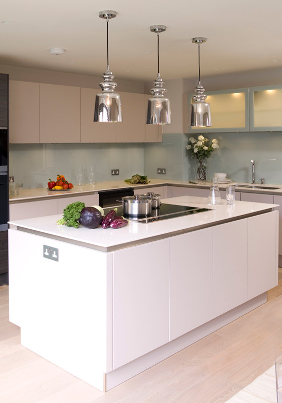 Mid-sized modern l-shaped eat-in kitchen in London with an undermount sink, flat-panel cabinets, beige cabinets, solid surface benchtops, white splashback, glass sheet splashback, black appliances, light hardwood floors and with island.
