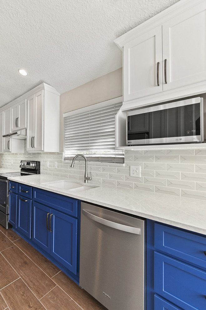 Inspiration for a large transitional l-shaped vinyl floor and brown floor open concept kitchen remodel in Jacksonville with an undermount sink, shaker cabinets, blue cabinets, quartzite countertops, white backsplash, ceramic backsplash, stainless steel appliances and a peninsula