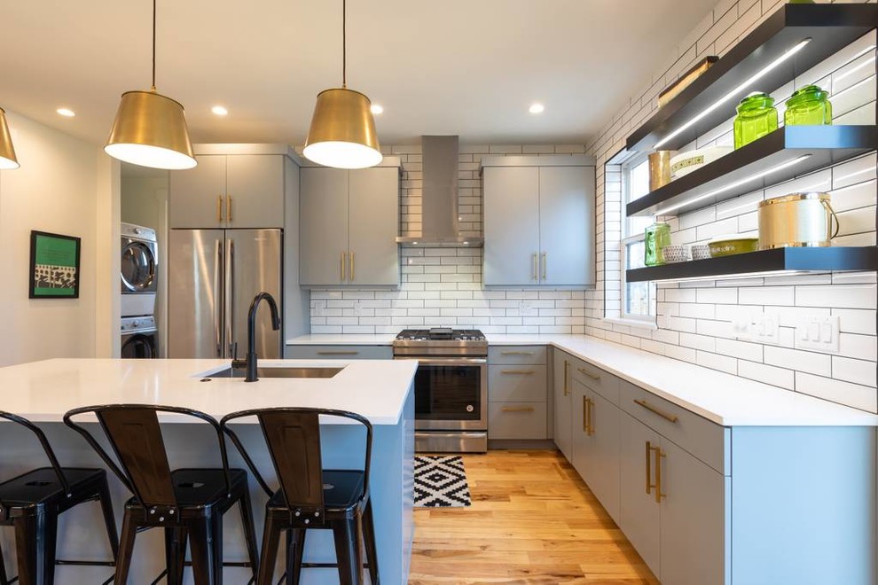 Country kitchen in Denver with a drop-in sink, flat-panel cabinets, grey cabinets, quartz benchtops, white splashback, ceramic splashback, stainless steel appliances, light hardwood floors, with island and white benchtop.