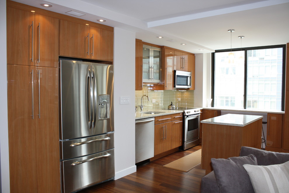 Photo of a small modern single-wall open plan kitchen in New York with stainless steel appliances, with island, an undermount sink, flat-panel cabinets, light wood cabinets, granite benchtops, green splashback, glass tile splashback and medium hardwood floors.