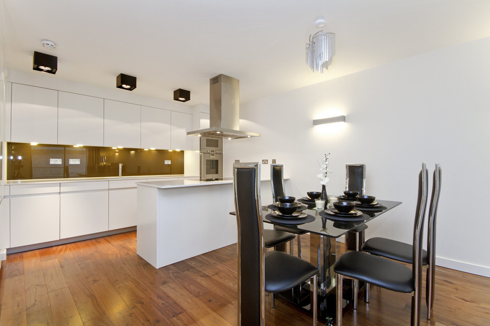 This is an example of a modern eat-in kitchen in London with stainless steel appliances, flat-panel cabinets, glass sheet splashback and brown splashback.