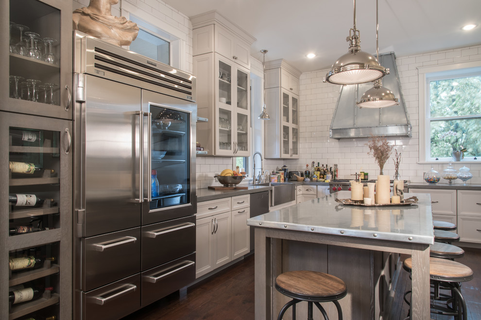 This is an example of a mid-sized industrial l-shaped separate kitchen in St Louis with a farmhouse sink, shaker cabinets, white cabinets, stainless steel benchtops, white splashback, subway tile splashback, stainless steel appliances, dark hardwood floors, with island and brown floor.