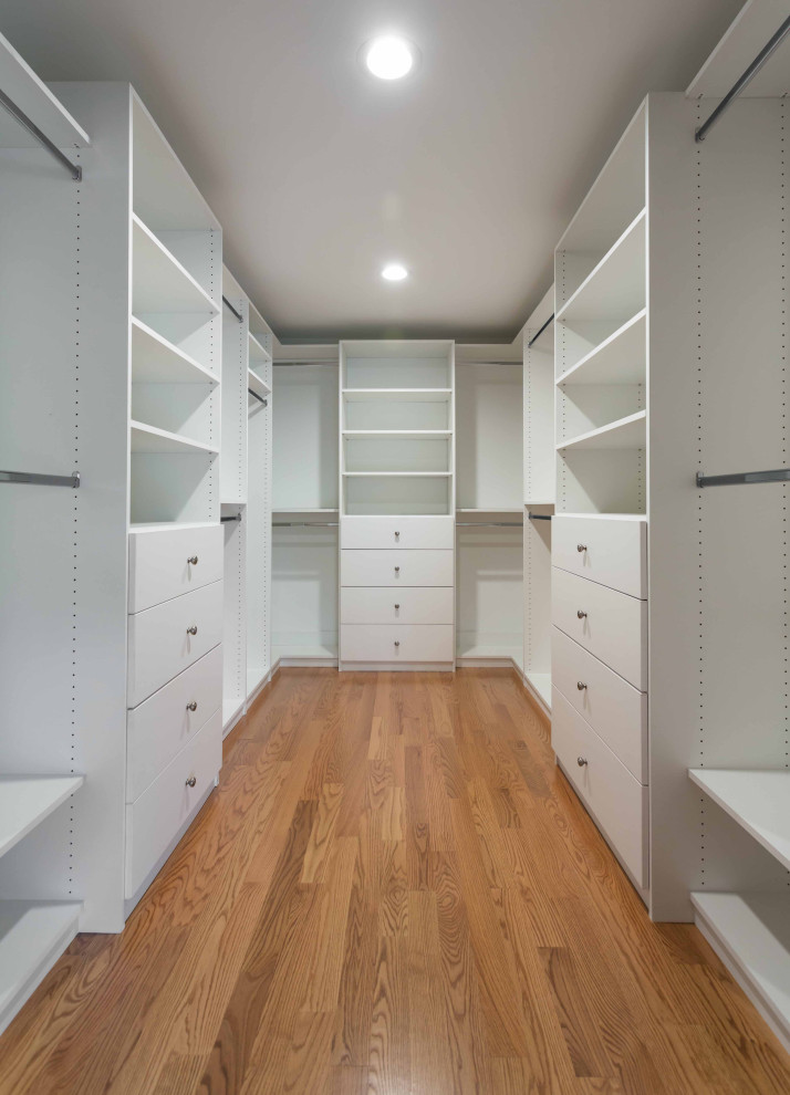 This is an example of an expansive arts and crafts gender-neutral walk-in wardrobe in Chicago with open cabinets, white cabinets, light hardwood floors, brown floor and wallpaper.