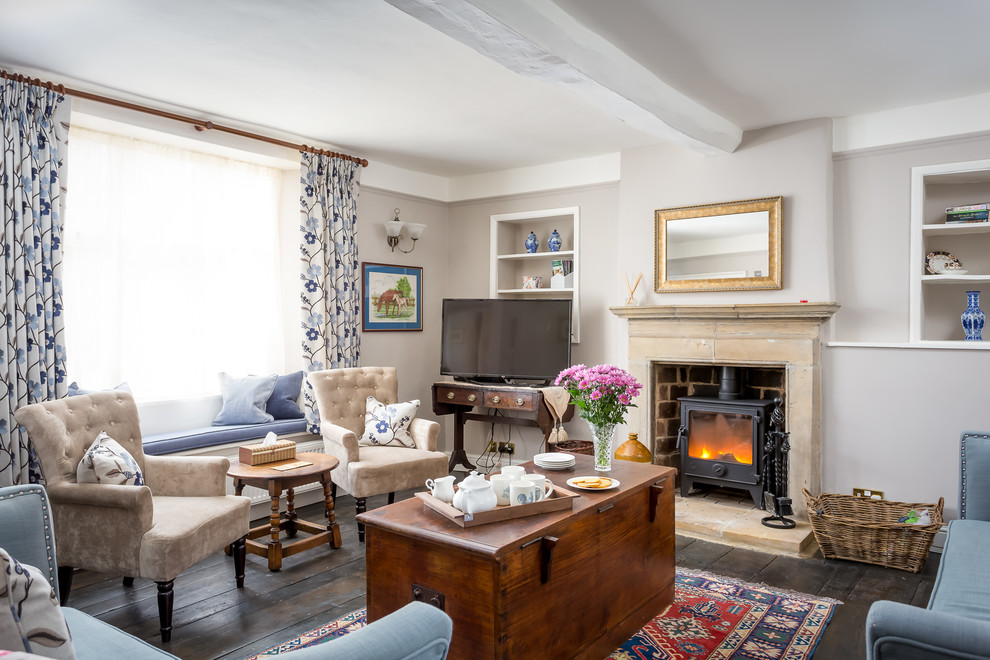 This is an example of a large country formal enclosed living room in Gloucestershire with dark hardwood floors, a wood stove, a stone fireplace surround, a freestanding tv, grey walls and brown floor.