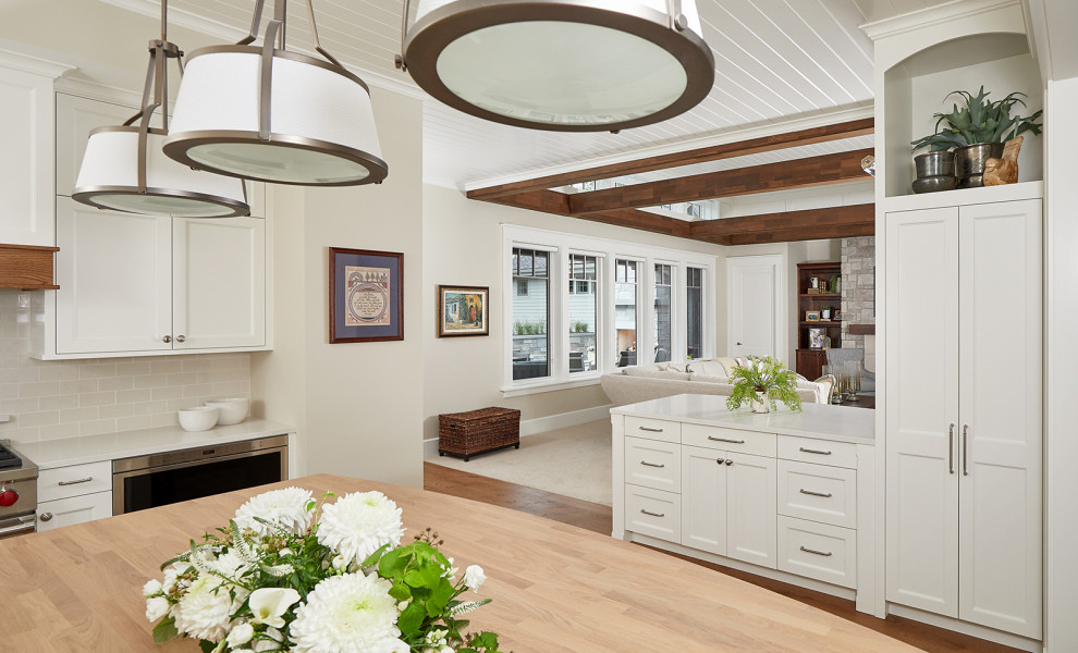 Inspiration for a traditional l-shaped eat-in kitchen in Grand Rapids with a farmhouse sink, shaker cabinets, white cabinets, quartz benchtops, beige splashback, ceramic splashback, panelled appliances, medium hardwood floors, with island, brown floor and white benchtop.