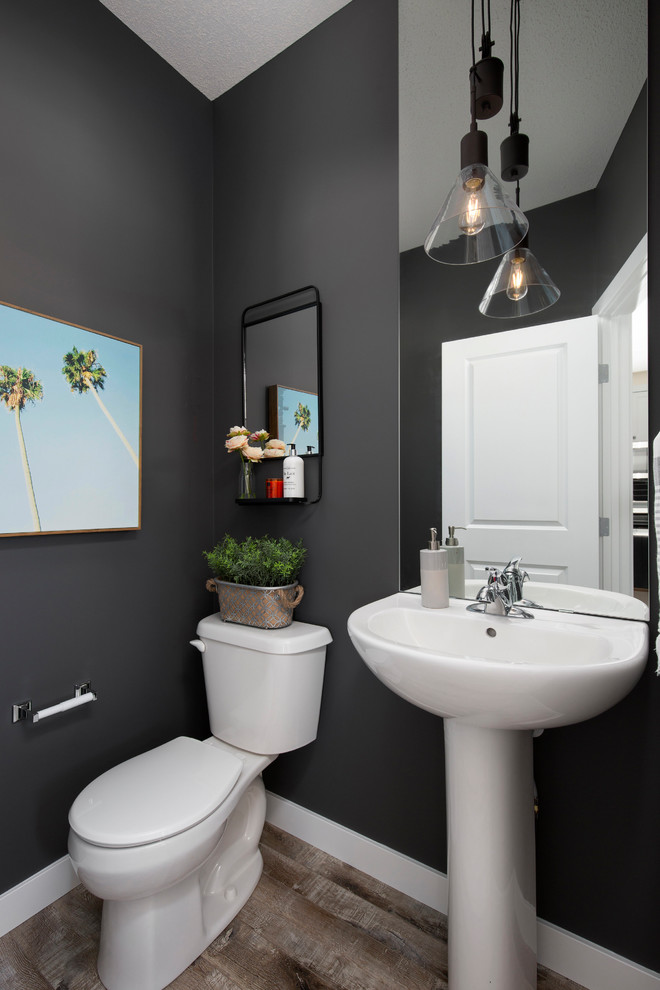 Photo of a small transitional powder room in Calgary with black walls, laminate floors, a pedestal sink, a two-piece toilet and brown floor.