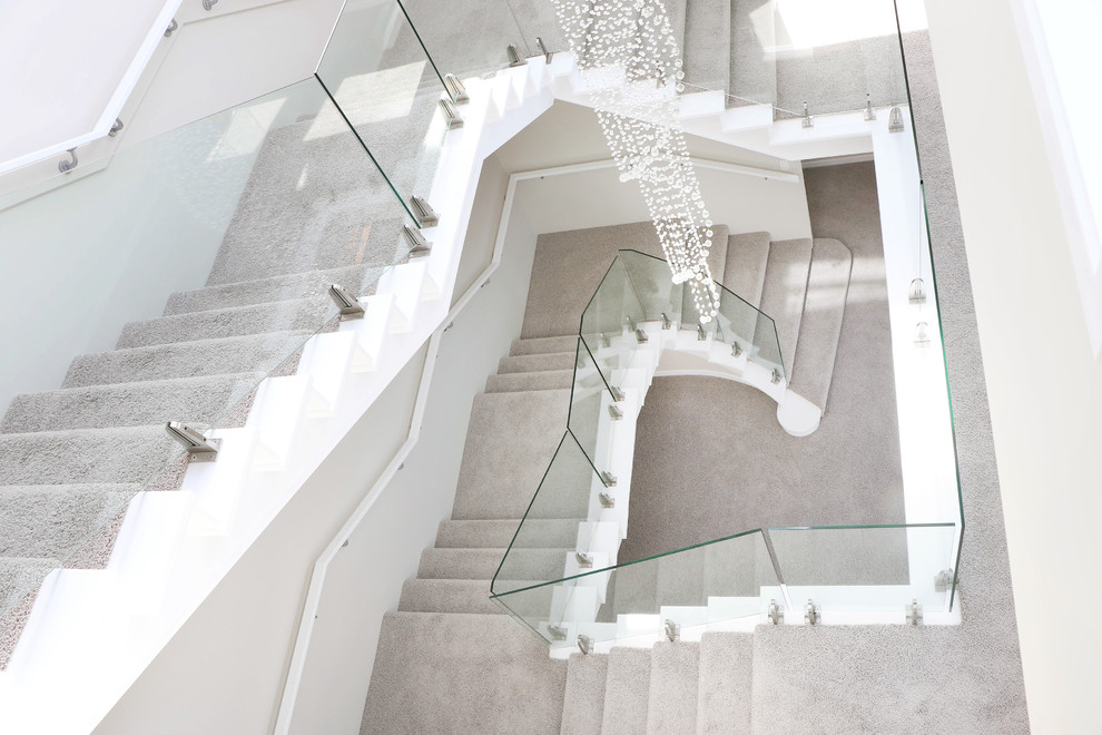 This is an example of an expansive traditional carpeted u-shaped staircase in Wellington with carpet risers and glass railing.