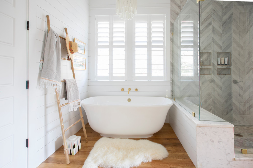Inspiration for a beach style master bathroom in Charleston with shaker cabinets, white cabinets, a freestanding tub, white walls, medium hardwood floors, an undermount sink, brown floor and white benchtops.