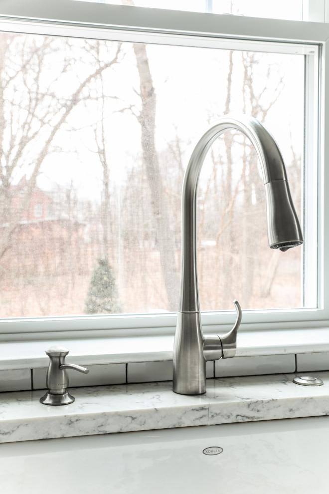 Example of a transitional l-shaped medium tone wood floor and brown floor eat-in kitchen design in Boston with a farmhouse sink, beaded inset cabinets, white cabinets, quartz countertops, white backsplash, subway tile backsplash, stainless steel appliances, an island and gray countertops
