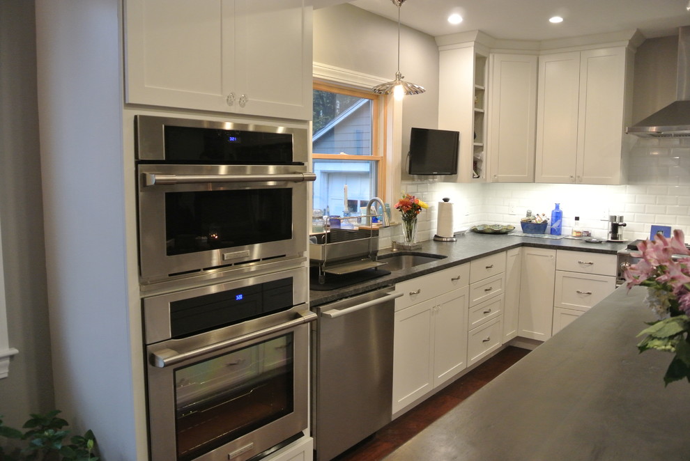 Example of a transitional medium tone wood floor kitchen design in Boston with shaker cabinets, white cabinets, granite countertops, white backsplash, subway tile backsplash, stainless steel appliances and an island