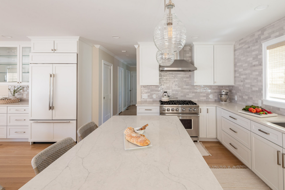 Inspiration for a huge transitional l-shaped light wood floor and brown floor open concept kitchen remodel in Boston with an undermount sink, shaker cabinets, white cabinets, quartz countertops, gray backsplash, subway tile backsplash, stainless steel appliances, an island and white countertops