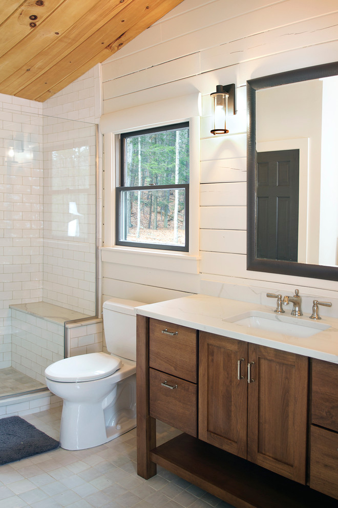 Photo of a large country master bathroom in New York with shaker cabinets, dark wood cabinets, an alcove shower, a two-piece toilet, white tile, white walls, an undermount sink, subway tile, porcelain floors, engineered quartz benchtops, grey floor, a hinged shower door and white benchtops.