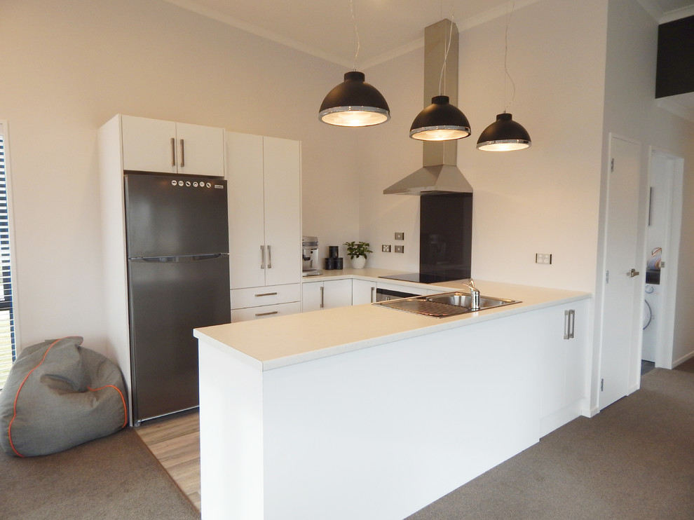Photo of a mid-sized modern u-shaped eat-in kitchen in Christchurch with flat-panel cabinets, white cabinets, laminate benchtops, black splashback, glass sheet splashback, stainless steel appliances and vinyl floors.