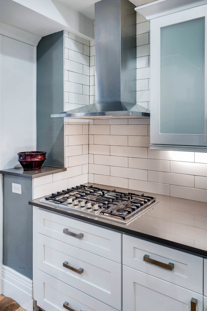 Example of a large mountain style light wood floor and brown floor eat-in kitchen design in Denver with a farmhouse sink, shaker cabinets, white cabinets, quartz countertops, white backsplash, ceramic backsplash, stainless steel appliances, a peninsula and brown countertops