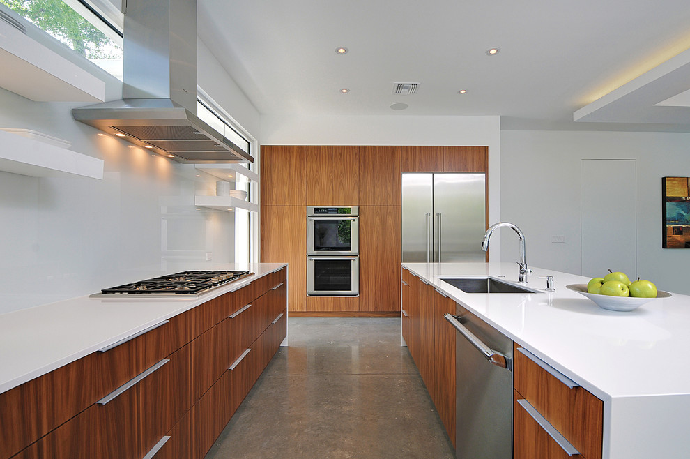 Photo of a contemporary galley open plan kitchen in Orlando with an undermount sink, flat-panel cabinets, medium wood cabinets, white splashback, glass sheet splashback, stainless steel appliances, concrete floors, with island and grey floor.