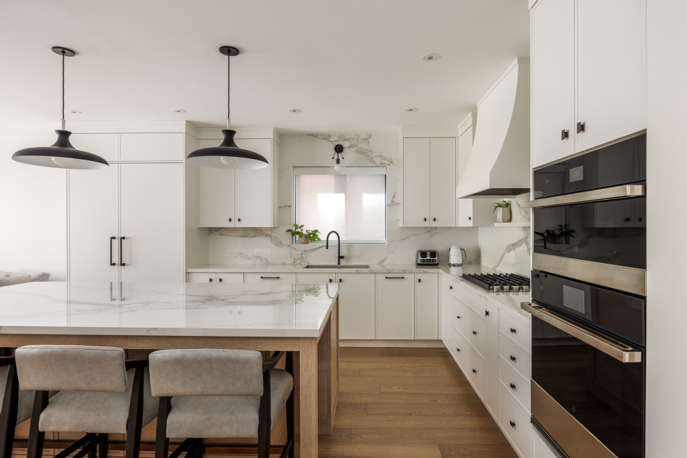 Transitional l-shaped medium tone wood floor and brown floor kitchen photo in Toronto with an undermount sink, shaker cabinets, white cabinets, white backsplash, stone slab backsplash, stainless steel appliances, an island and white countertops