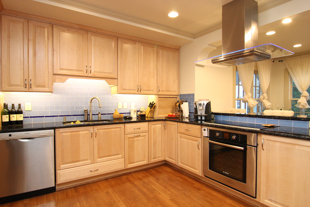 Huge transitional l-shaped medium tone wood floor open concept kitchen photo with an undermount sink, raised-panel cabinets, light wood cabinets, granite countertops, blue backsplash, glass tile backsplash and stainless steel appliances