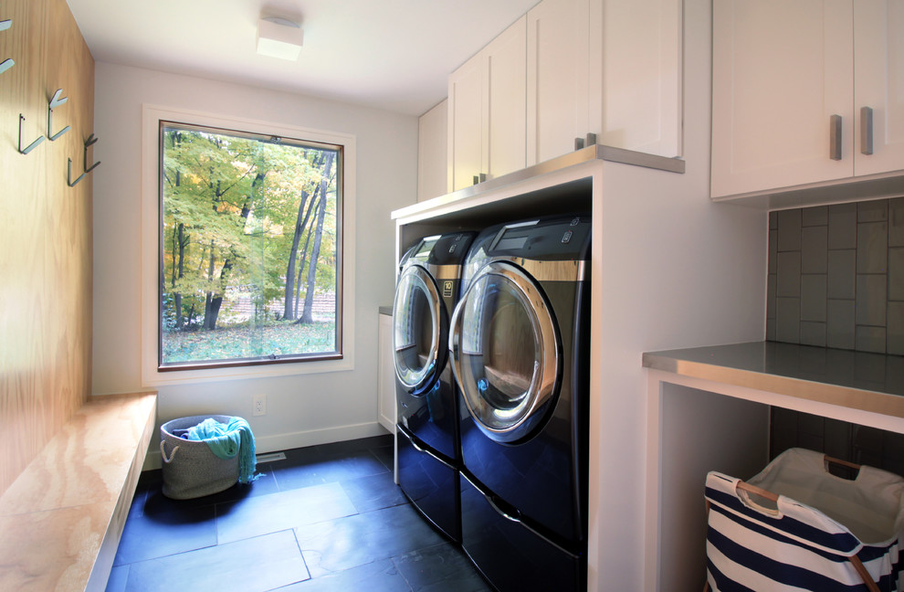 Photo of a small modern galley utility room in Minneapolis with a drop-in sink, shaker cabinets, white cabinets, stainless steel benchtops, white walls, slate floors, a side-by-side washer and dryer, grey floor and grey benchtop.