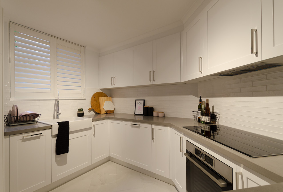 Small contemporary u-shaped eat-in kitchen in Sydney with a farmhouse sink, shaker cabinets, white cabinets, quartz benchtops, white splashback, ceramic splashback, stainless steel appliances and ceramic floors.