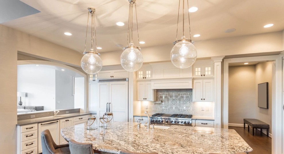Kitchen - large transitional l-shaped medium tone wood floor and brown floor kitchen idea in Seattle with a farmhouse sink, recessed-panel cabinets, white cabinets, granite countertops, gray backsplash, ceramic backsplash, paneled appliances, an island and multicolored countertops