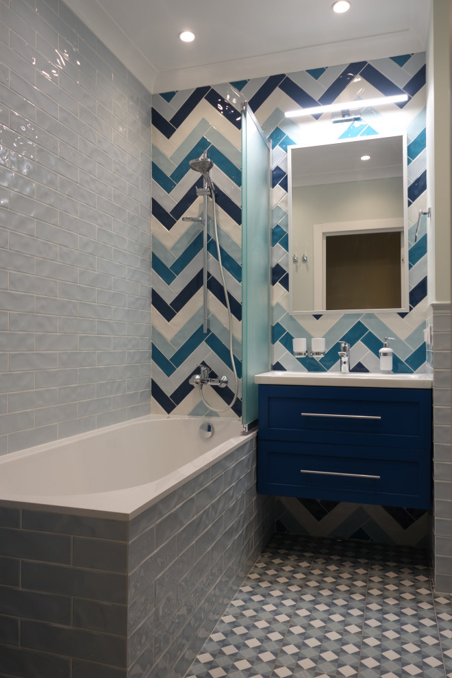 This is an example of a mid-sized beach style master bathroom in Moscow with raised-panel cabinets, blue cabinets, an undermount tub, a wall-mount toilet, blue tile, ceramic tile, blue walls, porcelain floors, a drop-in sink, solid surface benchtops, blue floor, white benchtops, a laundry, a single vanity, a floating vanity and recessed.