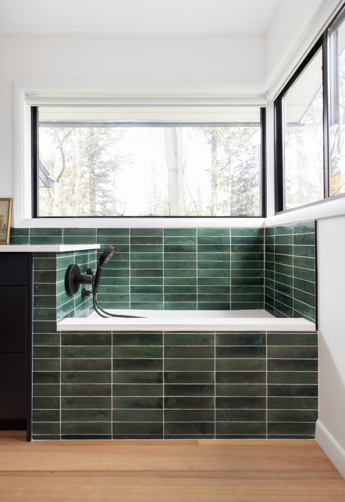 Design ideas for a mid-sized contemporary single-wall utility room in Portland with flat-panel cabinets, black cabinets, quartz benchtops, green splashback, cement tile splashback, white walls, light hardwood floors, a stacked washer and dryer and white benchtop.