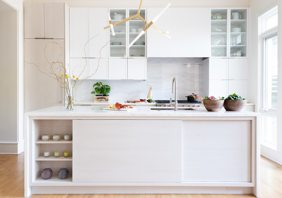 Photo of a mid-sized contemporary galley kitchen in DC Metro with flat-panel cabinets, marble benchtops, grey splashback, marble splashback, stainless steel appliances, with island, white benchtop, an undermount sink, white cabinets, light hardwood floors and beige floor.