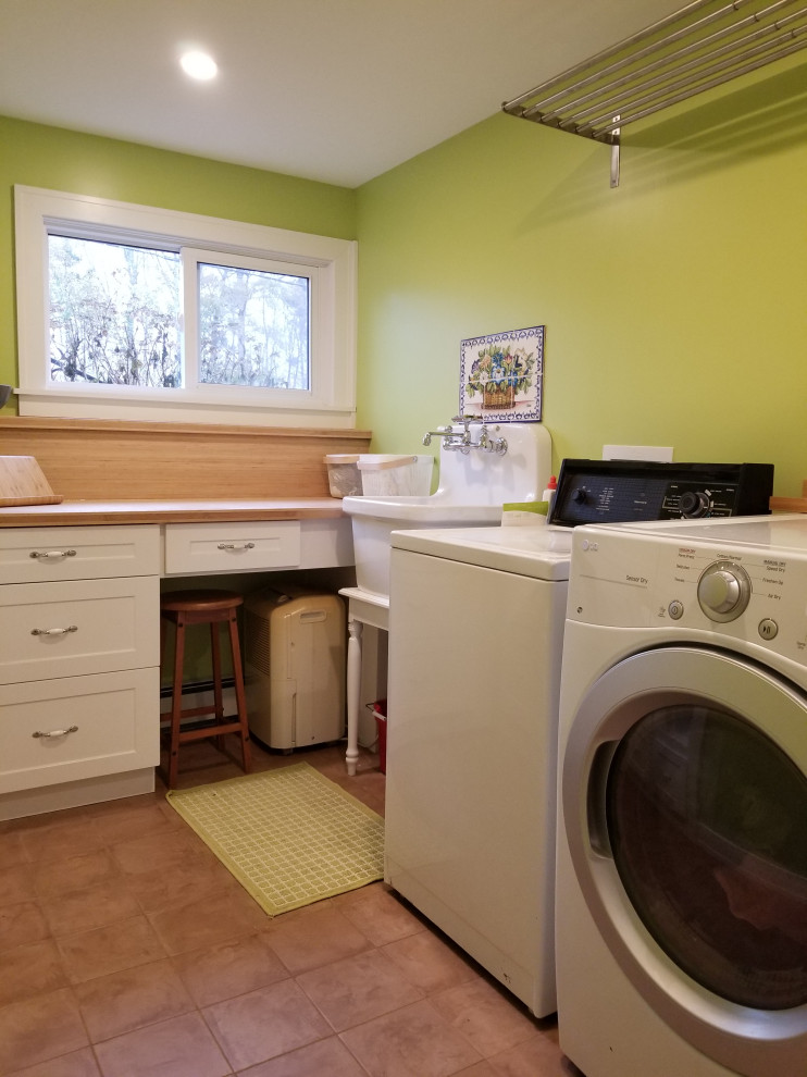 Design ideas for a mid-sized transitional l-shaped dedicated laundry room in Other with an utility sink, white cabinets, wood benchtops, green walls, porcelain floors, a side-by-side washer and dryer, brown floor, brown benchtop and shaker cabinets.