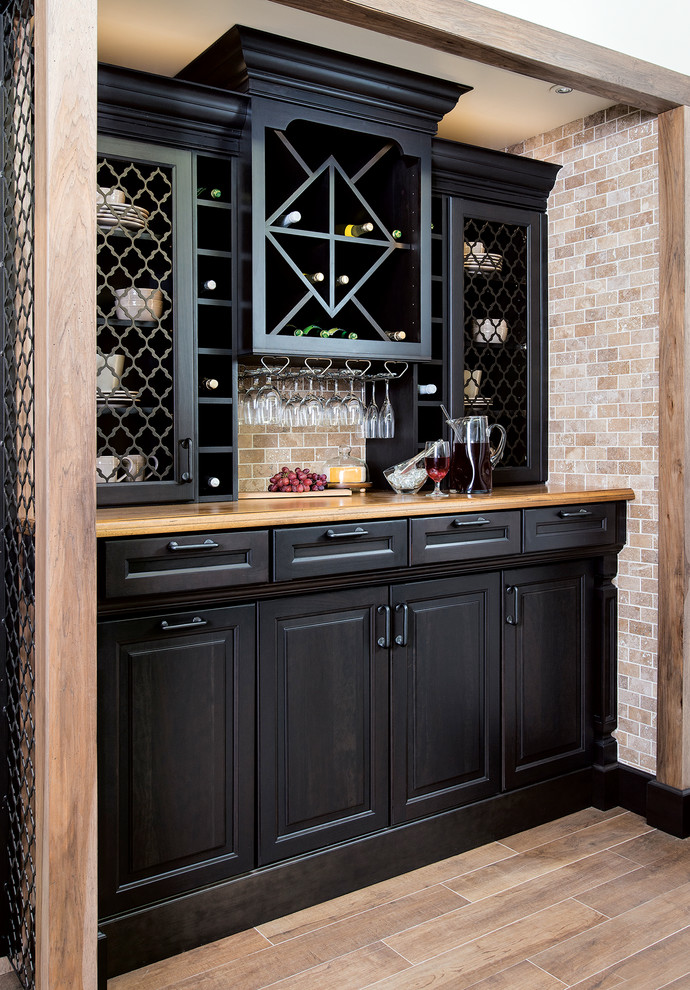 Inspiration for a small contemporary single-wall wet bar in St Louis with raised-panel cabinets, black cabinets, wood benchtops, beige splashback, stone tile splashback, porcelain floors, brown floor and brown benchtop.