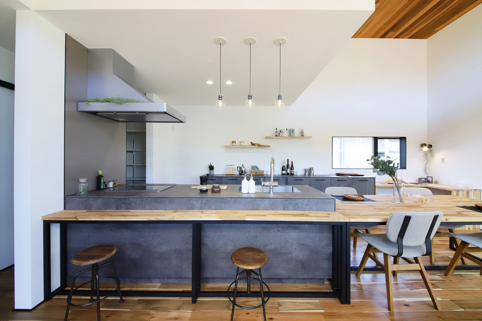 This is an example of an industrial single-wall eat-in kitchen in Other with an integrated sink, shaker cabinets, grey cabinets, tile benchtops, grey splashback, ceramic splashback, dark hardwood floors, a peninsula, brown floor, grey benchtop and wallpaper.