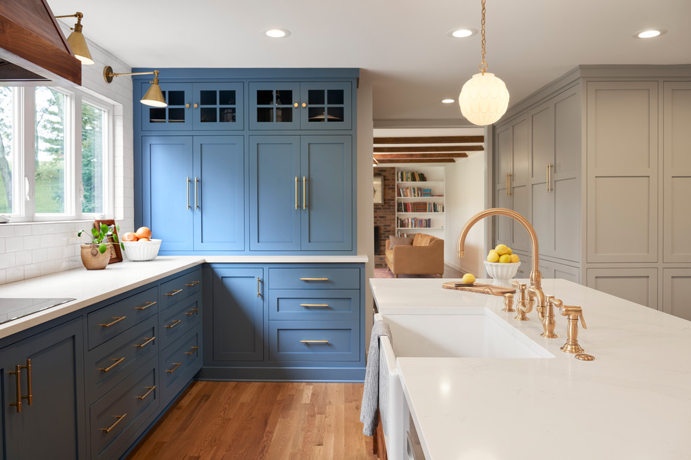 This is an example of a mid-sized midcentury u-shaped kitchen pantry in Nashville with a farmhouse sink, shaker cabinets, blue cabinets, quartzite benchtops, white splashback, ceramic splashback, stainless steel appliances, dark hardwood floors, with island, brown floor and white benchtop.