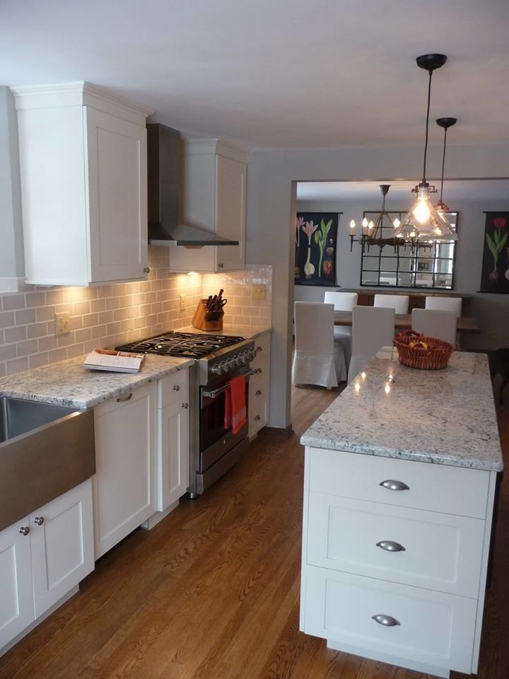 Large transitional u-shaped light wood floor eat-in kitchen photo in Milwaukee with a farmhouse sink, recessed-panel cabinets, white cabinets, granite countertops, gray backsplash, subway tile backsplash, stainless steel appliances and an island