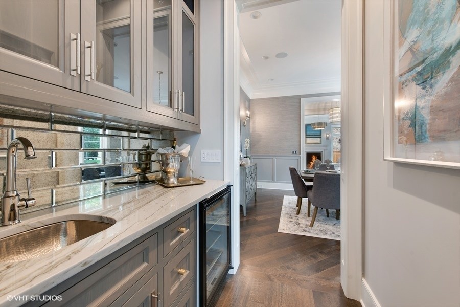 This is an example of a mid-sized transitional single-wall wet bar in Chicago with a drop-in sink, recessed-panel cabinets, grey cabinets, quartzite benchtops, grey splashback, mirror splashback, medium hardwood floors, brown floor and grey benchtop.