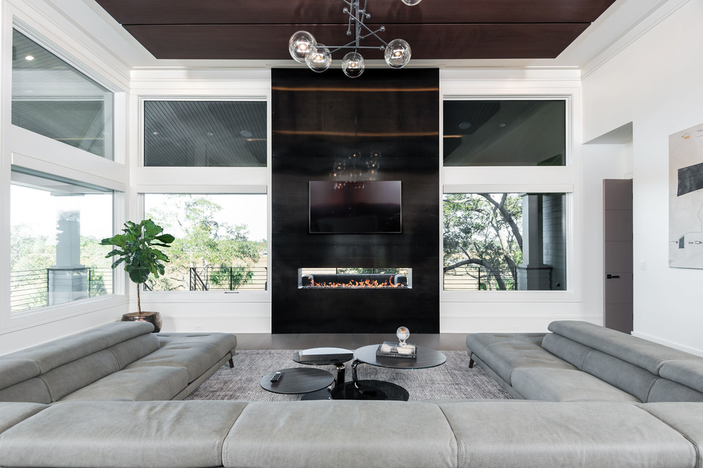 This is an example of a large contemporary open concept living room in Charleston with white walls, medium hardwood floors, a two-sided fireplace, a wall-mounted tv, brown floor and a metal fireplace surround.