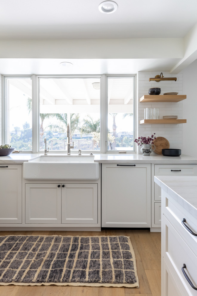 Design ideas for a classic u-shaped kitchen/diner in San Diego with a belfast sink, beaded cabinets, white cabinets, quartz worktops, white splashback, ceramic splashback and light hardwood flooring.