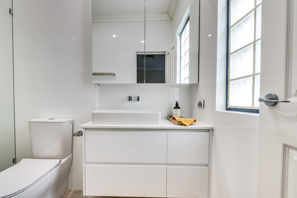 Inspiration for a contemporary bathroom in Perth with white cabinets, a one-piece toilet, white tile, white walls, porcelain floors, a drop-in sink, engineered quartz benchtops, multi-coloured floor and white benchtops.