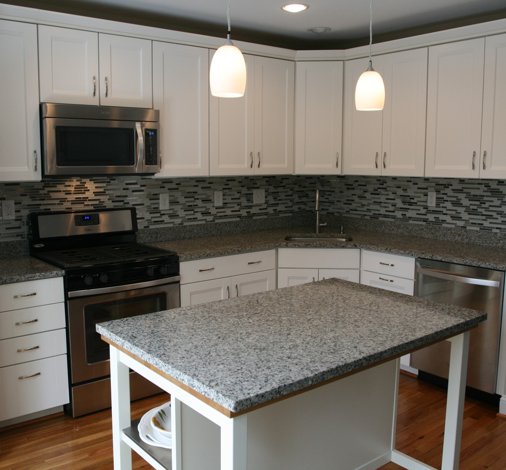 Mid-sized minimalist medium tone wood floor kitchen photo in Baltimore with an undermount sink, white cabinets, granite countertops, multicolored backsplash, glass tile backsplash and stainless steel appliances