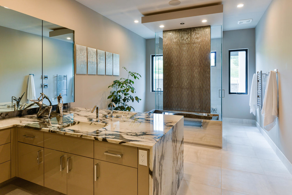 Inspiration for an expansive contemporary master bathroom in Denver with flat-panel cabinets, beige cabinets, an undermount tub, a curbless shower, brown tile, metal tile, grey walls, porcelain floors, an undermount sink, onyx benchtops, grey floor and an open shower.