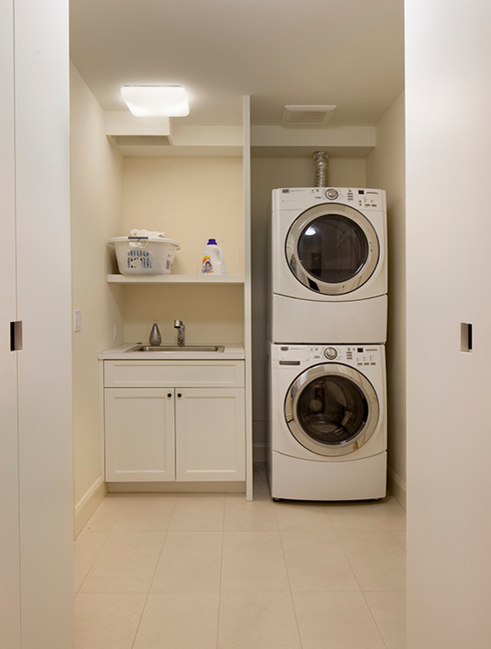 Photo of a mid-sized traditional single-wall dedicated laundry room in San Francisco with a drop-in sink, recessed-panel cabinets, white cabinets, laminate benchtops, beige walls, ceramic floors and a stacked washer and dryer.