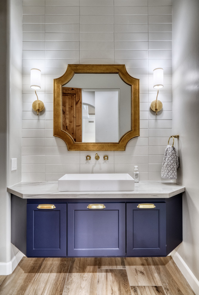 This is an example of a mid-sized transitional powder room in Phoenix with shaker cabinets, blue cabinets, a two-piece toilet, white tile, subway tile, white walls, porcelain floors, a vessel sink, quartzite benchtops, beige floor, white benchtops and a floating vanity.