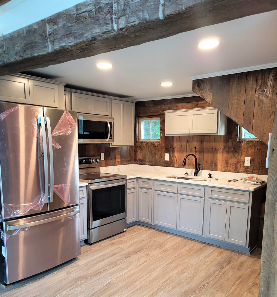 This is an example of a small rustic l-shaped enclosed kitchen in Boston with a submerged sink, shaker cabinets, grey cabinets, engineered stone countertops, white splashback, engineered quartz splashback, stainless steel appliances, vinyl flooring, no island, brown floors, white worktops and exposed beams.