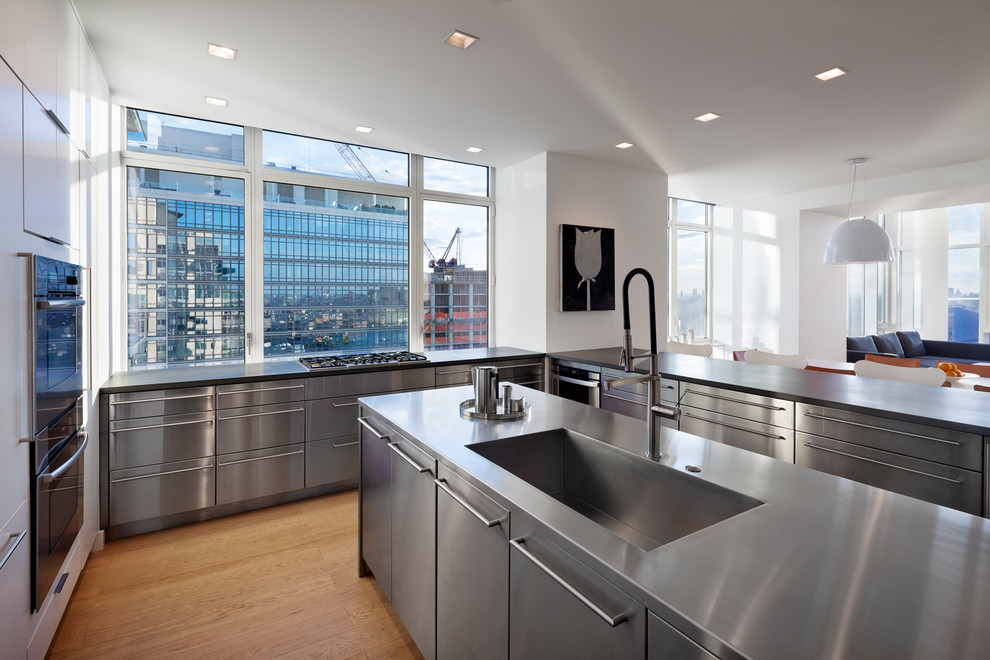 Inspiration for a large modern u-shaped eat-in kitchen in New York with an undermount sink, flat-panel cabinets, stainless steel cabinets, stainless steel benchtops, stainless steel appliances, light hardwood floors and with island.