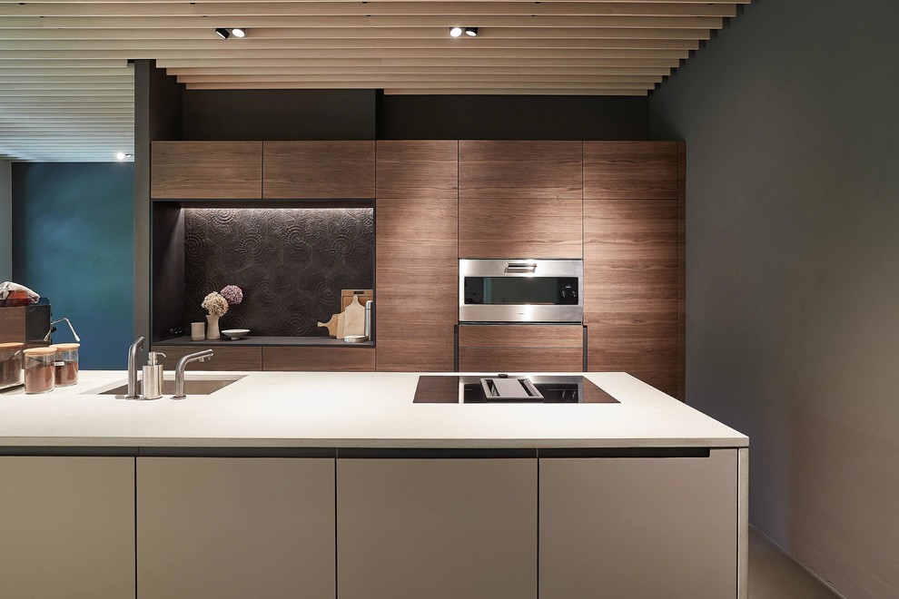 This is an example of a mid-sized contemporary galley eat-in kitchen in Stuttgart with an undermount sink, flat-panel cabinets, dark wood cabinets, black splashback, cement tile splashback, stainless steel appliances, with island, grey floor and grey benchtop.