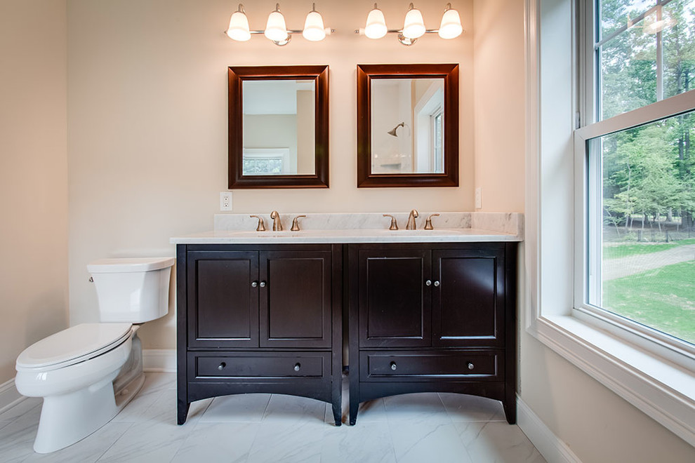 Example of a large transitional master marble floor and white floor drop-in bathtub design with shaker cabinets, black cabinets, beige walls, an undermount sink and marble countertops