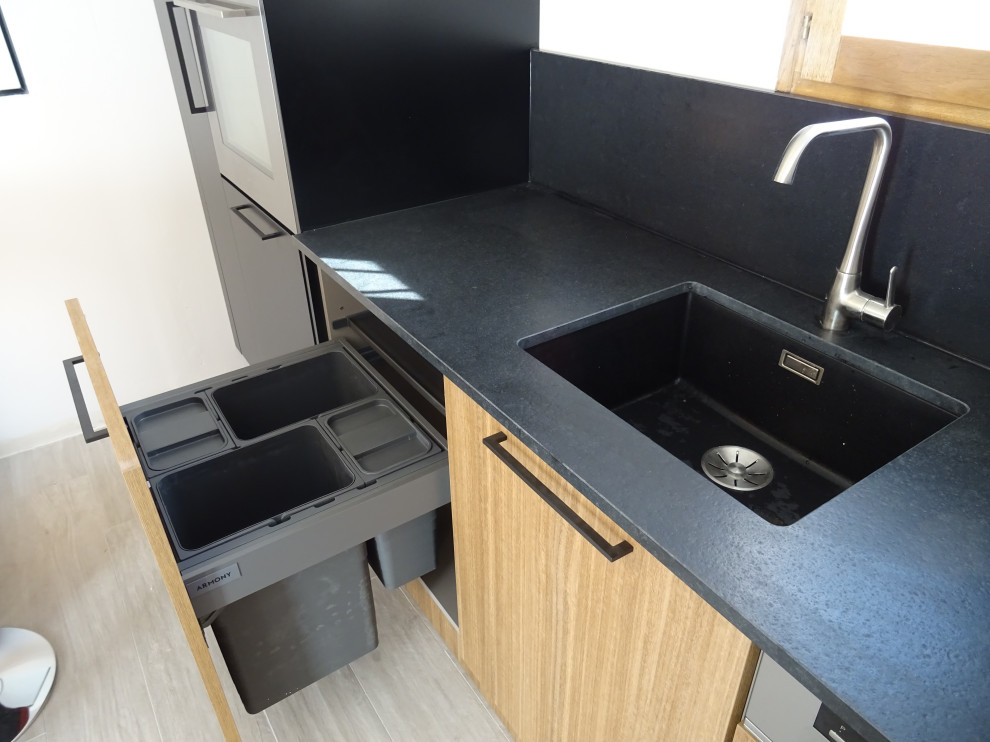 This is an example of a mid-sized industrial l-shaped separate kitchen in Marseille with an integrated sink, beaded inset cabinets, granite benchtops, black splashback, granite splashback, stainless steel appliances, ceramic floors, a peninsula, grey floor and black benchtop.