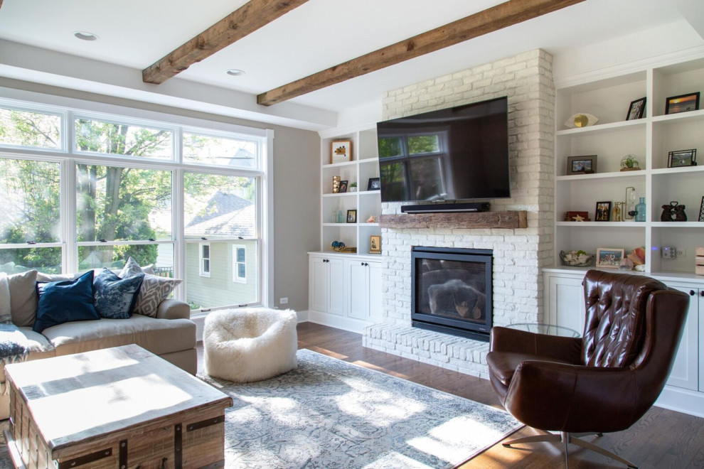 This is an example of a mid-sized country open concept family room in Chicago with grey walls, medium hardwood floors, a standard fireplace, a brick fireplace surround, a wall-mounted tv, brown floor, a home bar and exposed beam.