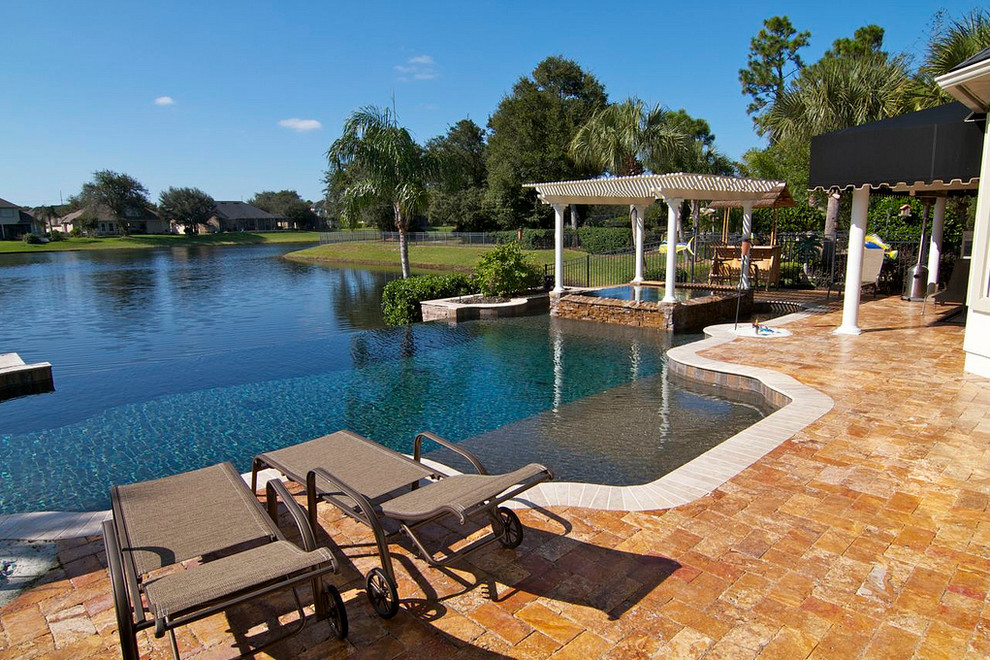 Example of a large backyard stone and custom-shaped infinity hot tub design in Jacksonville